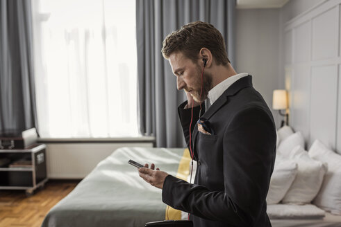 Seitenansicht eines Geschäftsmannes, der in einem Hotelzimmer sein Mobiltelefon abhört - MASF02089