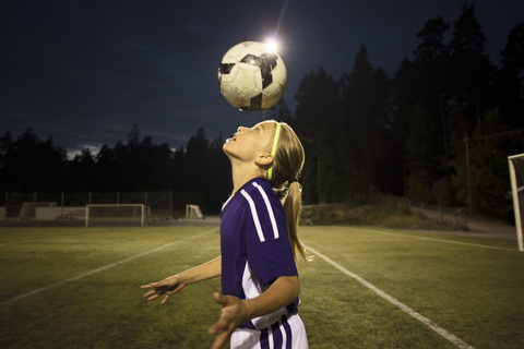 Side view of girl heading the ball on field against sky stock photo