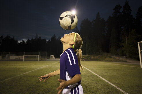 Seitenansicht eines Mädchens, das den Ball auf dem Feld gegen den Himmel köpft - MASF02092