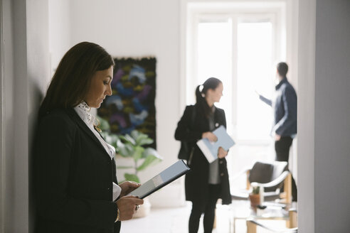 Side view of female realtor reading brochure with couple in background - MASF02093