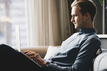 Side view of businessman using laptop at brightly lit office lobby - MASF02095