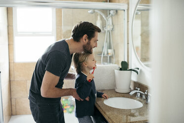 Side view of father watching daughter brushing teeth at sink in bathroom - MASF02101