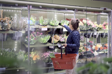 Seitenansicht einer Frau, die im Supermarkt Blumen aus einer Vitrine kauft - MASF02105