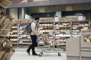 Seitenansicht eines Mannes, der mit einem Einkaufswagen durch einen Supermarkt geht und sich Brote ansieht - MASF02106