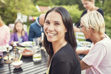 Porträt einer glücklichen Frau, die mit Familie und Freunden am Esstisch im Garten sitzt, während einer Gartenparty - MASF02114