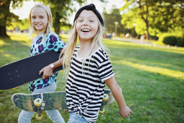 Porträt von glücklichen Freunden, die Skateboards tragen, während sie auf einer Wiese spazieren gehen - MASF02121