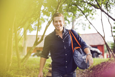 Portrait of smiling man carrying luggage on steps at back yard - MASF02122