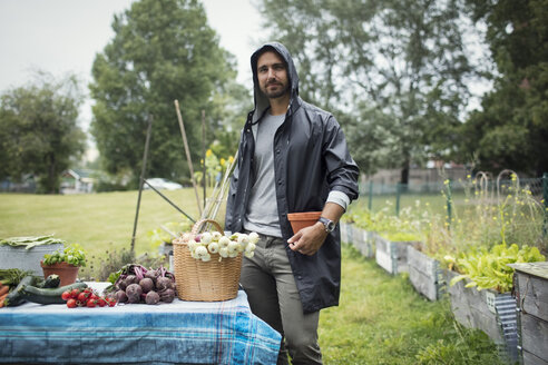 Portrait of mid adult man standing by freshly harvested vegetables on table at urban garden - MASF02129