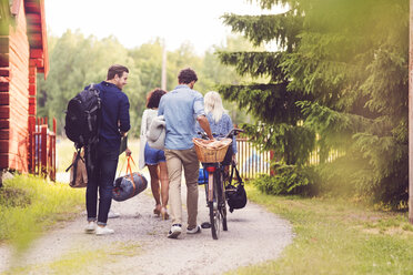 Rear view of friends walking with bicycle and luggage on footpath by trees - MASF02164