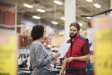 Salesman discussing with female customer holding document in hardware store stock photo