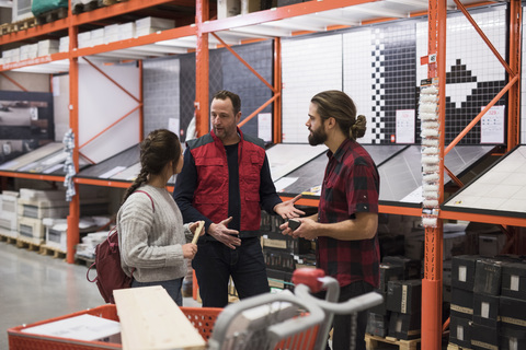 Salesman discussing with couple by shelves at hardware store stock photo