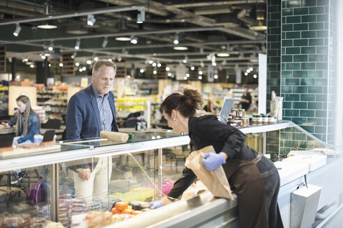 Verkäuferin verkauft Lebensmittel an einen reifen Mann in einem Bio-Supermarkt - MASF02175
