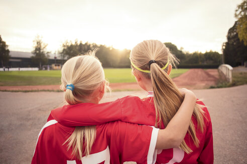 Rückansicht von weiblichen Fußballfreunden, die auf einem Fußweg stehen und bei Sonnenuntergang auf ein Feld schauen - MASF02183
