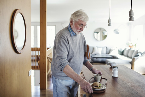 Älterer Mann hält Frühstück im Tablett zu Hause, lizenzfreies Stockfoto