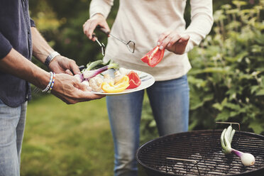 Mittelteil eines Vaters und einer Tochter, die Gemüse auf einem Grill im Hinterhof zubereiten - MASF02196