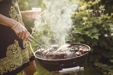 Midsection of woman grilling meat on barbecue in back yard - MASF02200