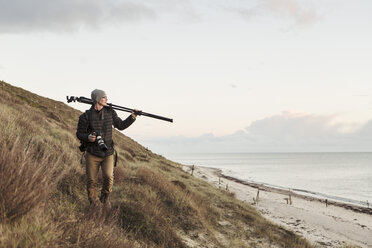 Photographer looking away while carrying tripod on hill by sea - MASF02215