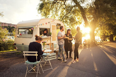 Owner looking at customers standing on street through food truck window - MASF02216