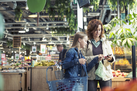 Mutter und Tochter benutzen ein Smartphone in einem Bioladen, lizenzfreies Stockfoto