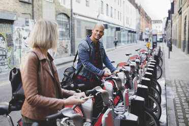 Multi-ethnic couple renting bicycles from bike share stand in city - MASF02227