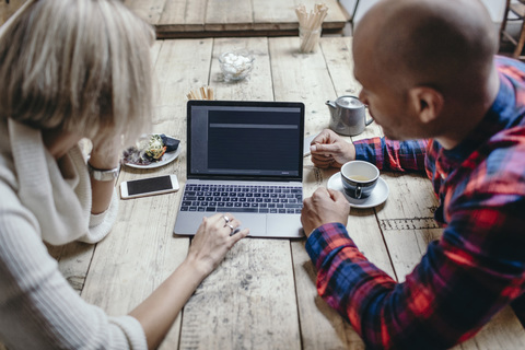 Multiethnisches Paar mit Laptop am Tisch in einem Café, lizenzfreies Stockfoto