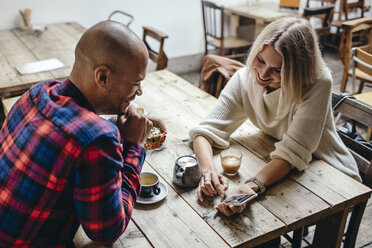 Multi-ethnic couple using mobile phone at table in coffee shop - MASF02230