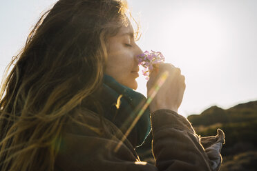 Woman in sunlight enjoying fragrance of a flower - KKAF00939