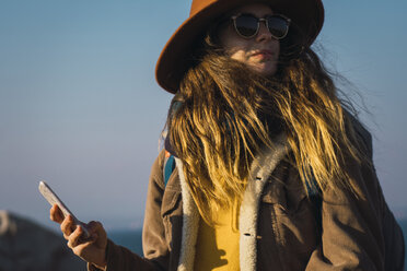 Italy, Sardinia, woman on a hiking trip with cell phone looking around - KKAF00949