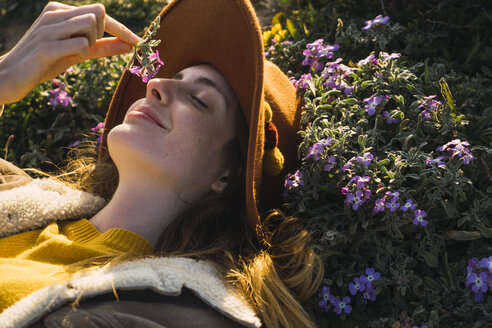 Woman lying in meadow enjoying fragrance of a flower - KKAF00951