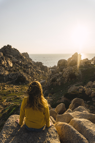 Italien, Sardinien, Frau auf Wanderschaft, sitzend auf einem Felsen an der Küste, lizenzfreies Stockfoto