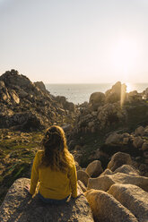 Italien, Sardinien, Frau auf Wanderschaft, sitzend auf einem Felsen an der Küste - KKAF00957