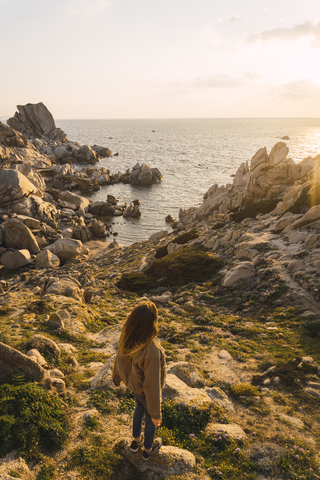 Italien, Sardinien, Frau beim Wandern auf einem Felsen an der Küste stehend, lizenzfreies Stockfoto