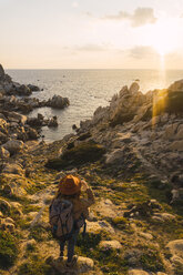 Italy, Sardinia, woman on a hiking trip standing on rock at the coast - KKAF00963