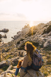 Italien, Sardinien, Frau auf Wanderschaft, sitzend auf einem Felsen an der Küste - KKAF00965