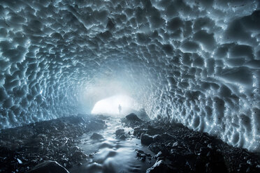 Entfernte Ansicht eines Mannes, der in einer eisbedeckten Höhle auf einem Felsen steht - CAVF35677