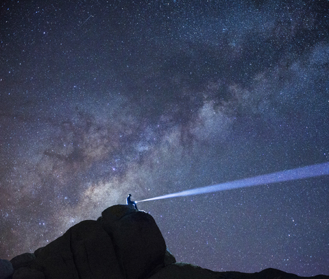 Niedriger Blickwinkel von Wanderer mit beleuchteter Taschenlampe gegen Sternenhimmel, lizenzfreies Stockfoto