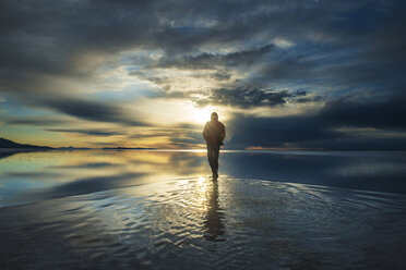 Full length of man standing on salt flat against cloudy sky during sunset - CAVF35682