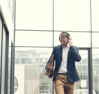 Smiling businessman listening to music with headphones - UUF13268