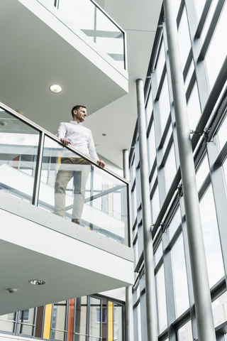 Geschäftsmann in einem Bürogebäude, der sich auf ein Geländer stützt, lizenzfreies Stockfoto
