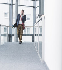 Smiling businessman holding skateboard and talking on cell phone - UUF13289