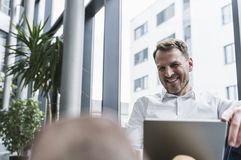 Porträt eines lächelnden Geschäftsmannes mit Laptop in einer Bürolounge, lizenzfreies Stockfoto