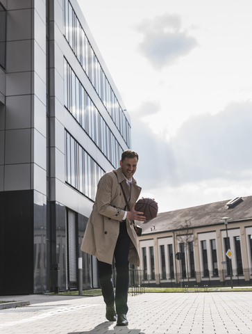 Happy businessman playing basketball outside office building stock photo