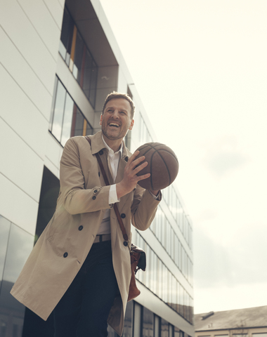 Happy businessman playing basketball outside office building stock photo