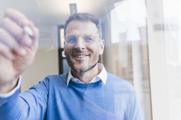 Confident businessman writing on glass pane - UUF13303