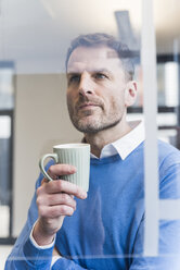 Fokussierter Geschäftsmann, der eine Tasse Kaffee hält und auf eine Glasscheibe schaut - UUF13304