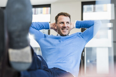 Lächelnder, lässiger Geschäftsmann im Büro, der sich zurücklehnt - UUF13307