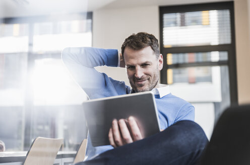 Lächelnder Geschäftsmann mit Tablet im Büro - UUF13308