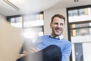 Lächelnder Geschäftsmann mit Tablet im Büro - UUF13309