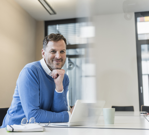 Porträt eines lächelnden Geschäftsmannes mit Laptop im Büro, lizenzfreies Stockfoto