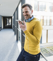 Lässig lächelnder Geschäftsmann im Büro mit Smartphone - UUF13313